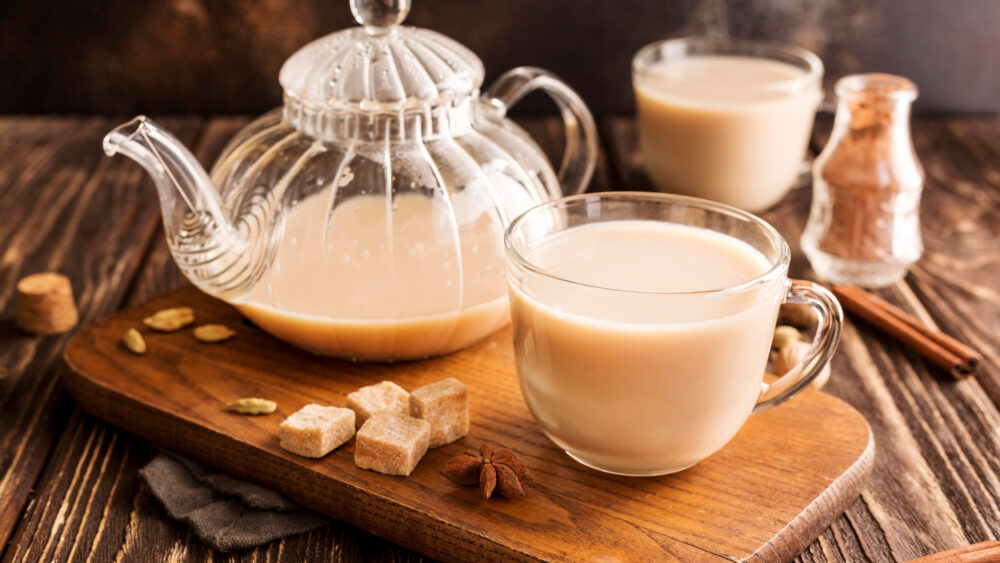 A glass of warm teh tarik with a smooth frothy top, accompanied by a cinnamon stick on a wooden table is a traditional drink with rich flavor and an enticing aroma.
