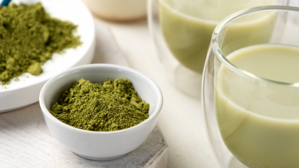 A cup of green matcha tea with matcha powder beside it, showcasing its vibrant green color and calming signature aroma.