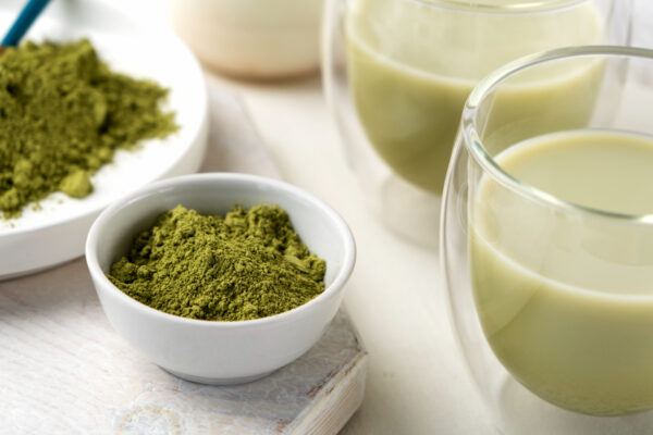 A cup of green matcha tea with matcha powder beside it, showcasing its vibrant green color and calming signature aroma.