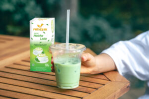 iced matcha latte in a plastic cup with prendjak matcha in the back